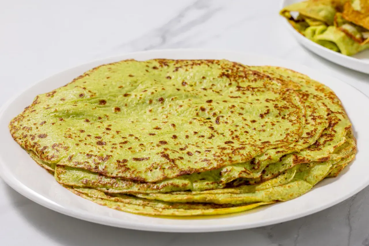 Piatto di crepes di zucchine verdi, sottili e leggermente dorate, impilate su un piatto bianco.