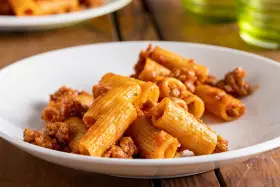 Rigatoni conditi con un ricco ragù di salsiccia, serviti su un piatto bianco.