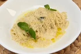 Spaghetti al limone cremosi, cosparsi di parmigiano e guarniti con foglie di menta fresca. Un piatto profumato e invitante.