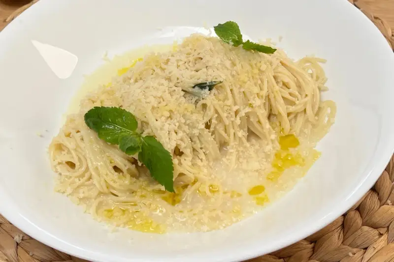 Spaghetti al limone cremosi, cosparsi di parmigiano e guarniti con foglie di menta fresca. Un piatto profumato e invitante.