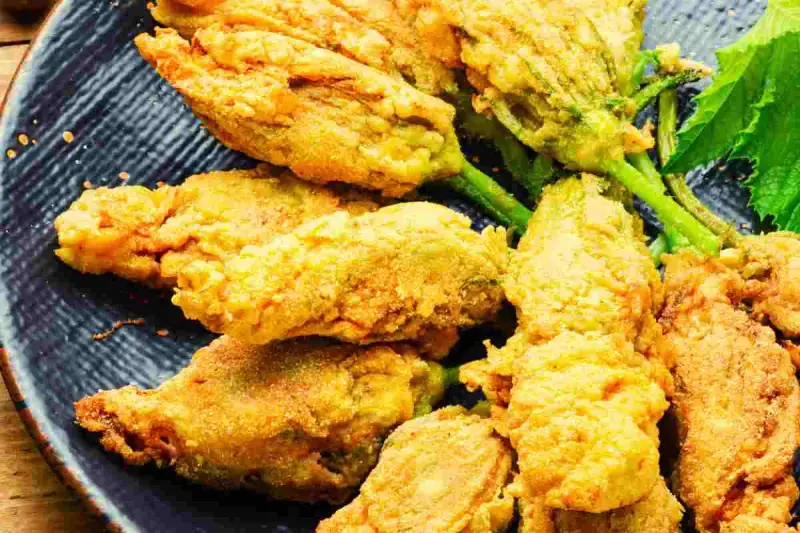 Fiori di zucca ripieni dorati e croccanti, serviti su un piatto blu scuro.