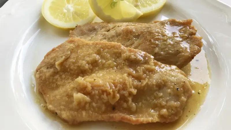 Deliziose scaloppine al limone, succulente e dorate, servite con spicchi di limone fresco.