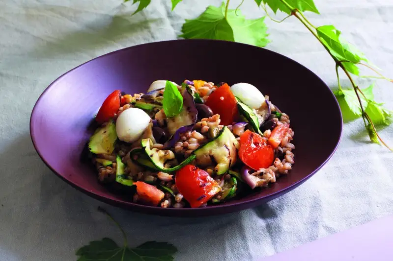 Deliziosa insalata di farro estiva con verdure grigliate, pomodorini, mozzarelline e basilico fresco.