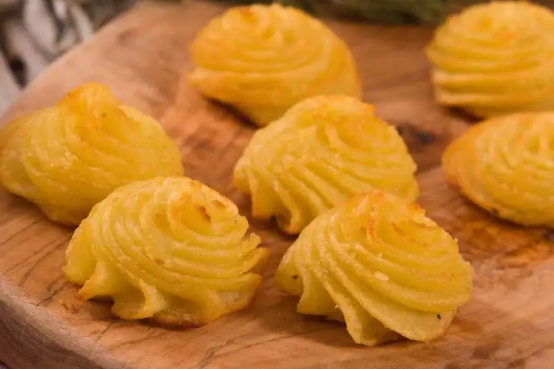 Patate duchessa dorate e invitanti, disposte su un tagliere di legno, pronte per essere gustate.